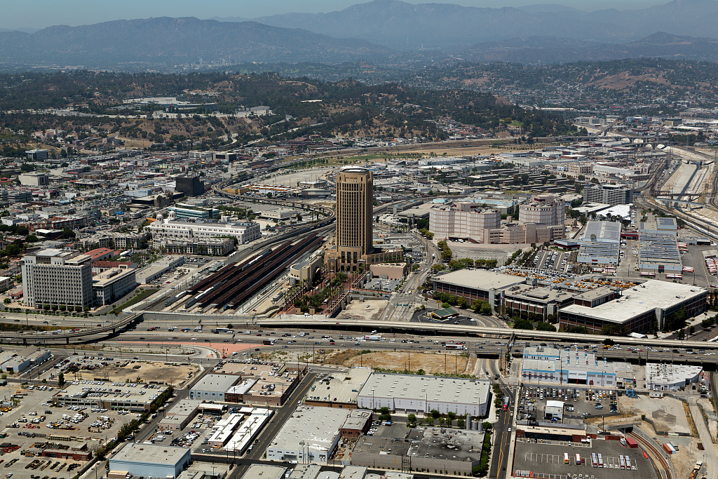 Aerial view of city streets and freeways beneath distant hills.