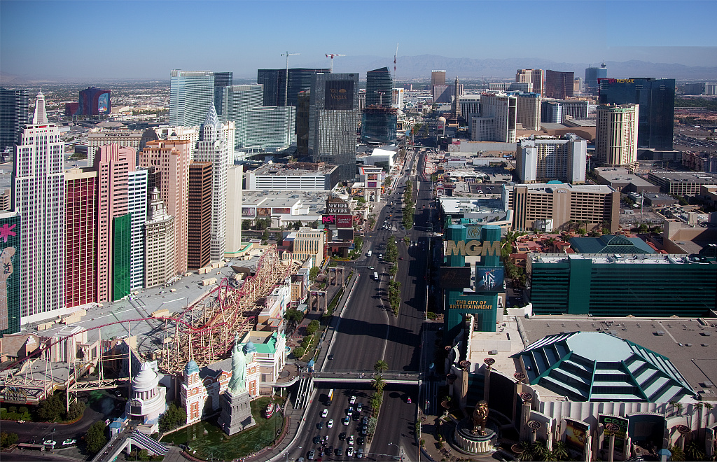 Aerial view along a broad avenue, with towers and desert mountains.